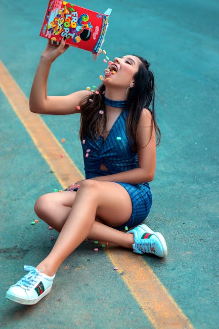 Stylish woman sitting on a road, playfully pouring cereal into her mouth in a fun, carefree moment.